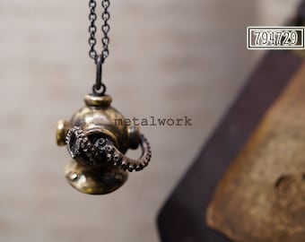 May include: A brass pendant necklace featuring a detailed sculpture of a diving helmet with an octopus attached. The necklace has a black chain.