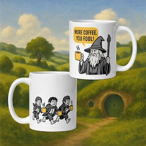 Puede incluir: Dos tazas de café de cerámica blanca con ilustraciones de dibujos animados. Una taza presenta un mago con el texto "MORE COFFEE, YOU FOOL!". La otra taza muestra tres figuras corriendo con tazas de café. El fondo es un paisaje verde.