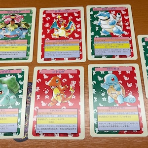 Puede incluir: Una colección de siete tarjetas coleccionables rectangulares con ilustraciones coloridas de varias criaturas. Cada tarjeta muestra un personaje en la parte superior, seguido de texto en japonés y un fondo con patrones rojos y verdes.