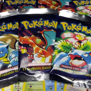 May include: Several Pok&eacute;mon Trading Card Game booster packs with various Pok&eacute;mon characters on the front. The packs are sealed and feature the Pok&eacute;mon logo. Some individual cards are visible in the foreground.