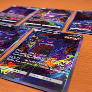 Op de afbeelding: Vijf Gengar-verzamelkaarten met levendige paarse, blauwe en neonkleurige verfspatten. Elke kaart toont het personage Gengar met rode ogen en een wijde mond. De tekst op de kaarten bevat Gengar VMAX, Single Strike en beschrijvingen van aanvallen.