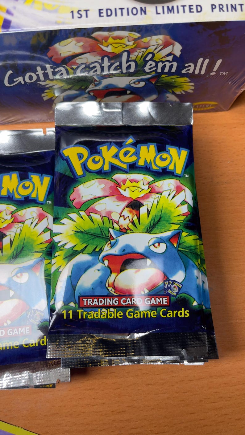 May include: Sealed Pok&eacute;mon trading card game pack. The pack features the Pok&eacute;mon logo in yellow and blue, with a blue and red creature illustration. The text "11 Tradable Game Cards" is visible. The packaging is silver and blue.