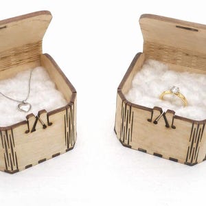 Two handcrafted wooden gift boxes sit open, each lined with soft white cotton to show how they can present small keepsakes. The laser‑cut joints, engraved details, and natural wood grain highlight the box’s craftsmanship. Jewelry shown is for display only, demonstrating how the boxes can be used for gifting or storage.