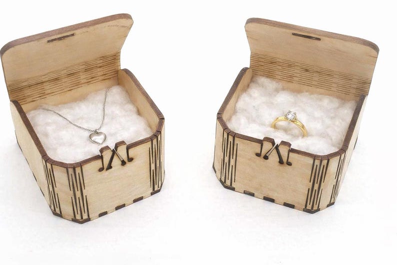 Two handcrafted wooden gift boxes sit open, each lined with soft white cotton to show how they can present small keepsakes. The laser‑cut joints, engraved details, and natural wood grain highlight the box’s craftsmanship. Jewelry shown is for display only, demonstrating how the boxes can be used for gifting or storage.