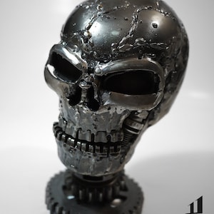May include: A metal skull sculpture with a gear base. The skull is made of welded metal and has a distressed silver finish. The sculpture is approximately 8 inches tall.