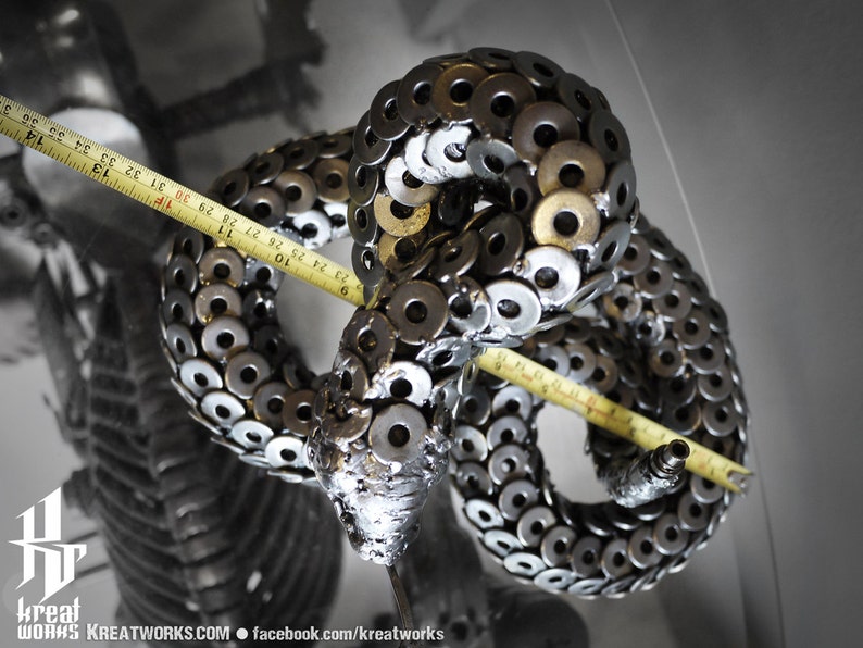 May include: A metal sculpture of a snake made from hundreds of silver and gold washers. The snake is coiled and measures approximately 91 cm in length.