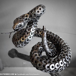 May include: A silver metal sculpture of a rattlesnake, crafted from numerous metal washers. The snake is coiled in a defensive posture with its head raised.