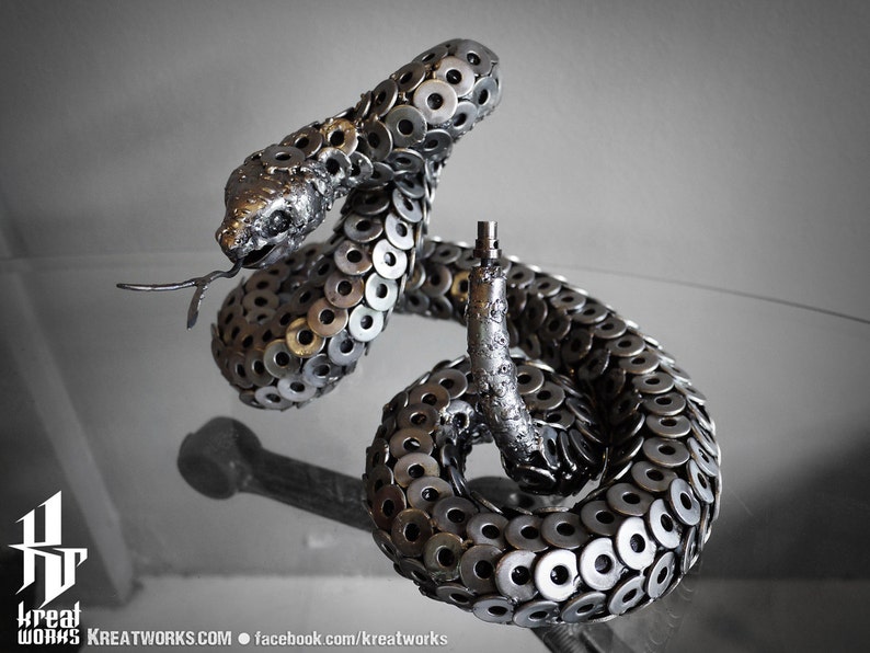 May include: A silver metal sculpture of a rattlesnake, crafted from numerous metal washers. The snake is coiled in a defensive posture with its head raised.