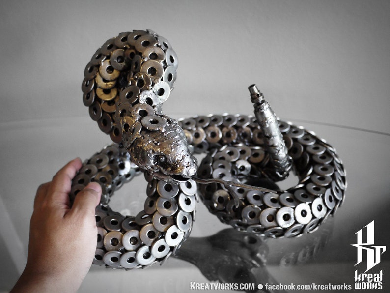 May include: A silver metal sculpture of a rattlesnake, crafted from numerous metal washers. The snake is coiled in a striking pose, with its head raised and its tail curled.
