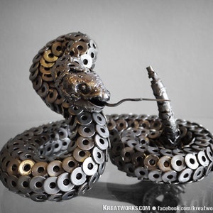 May include: A silver metal sculpture of a rattlesnake, crafted from numerous metal washers. The snake is coiled in a defensive posture, with its head raised and its tail curled.