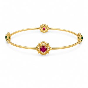 May include: A thin gold bangle bracelet featuring four ornate, filigree-style circular settings. Two settings contain vibrant round red stones, while the other two settings contain round green stones, all evenly spaced along the polished gold band.