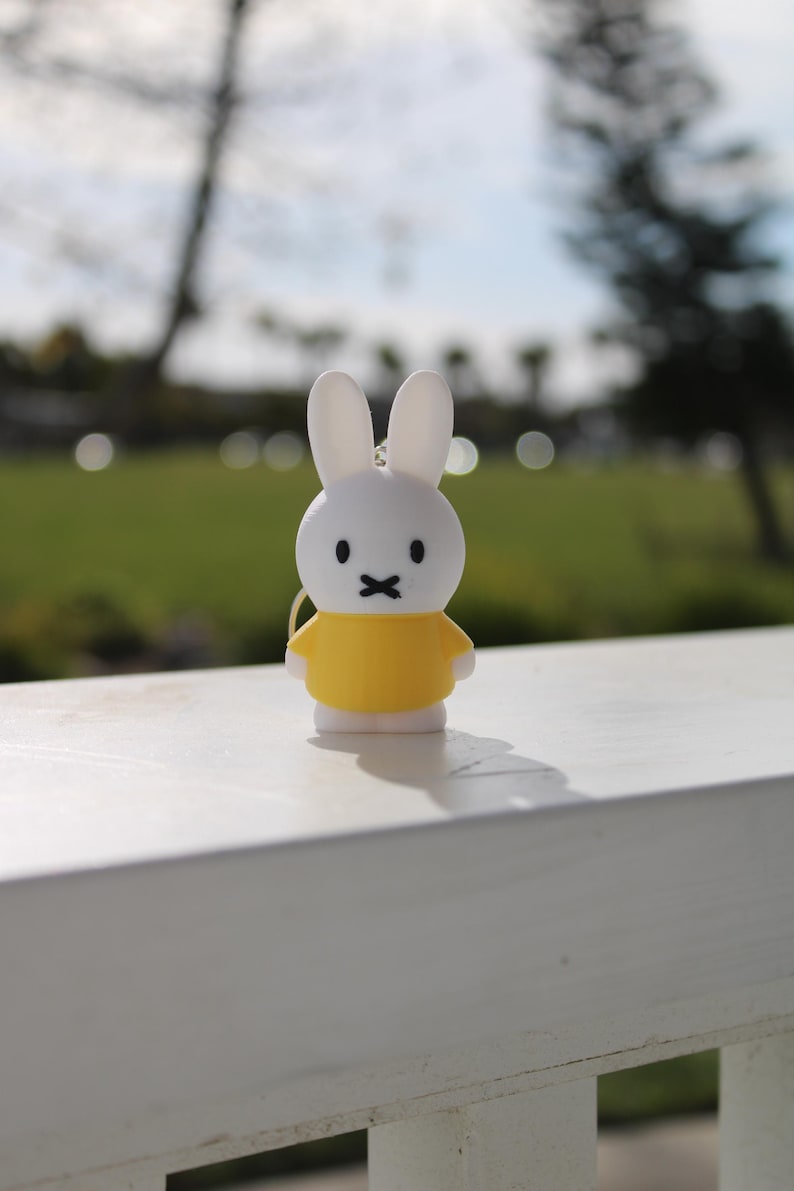 Pode incluir: Uma figura de coelho branco vestindo uma camisa amarela. A figura est&aacute; sentada em uma superf&iacute;cie de madeira branca.