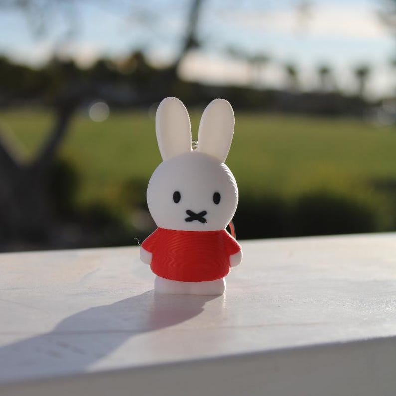 Pode incluir: Uma figura de coelho branco vestindo uma camisa vermelha. O coelho tem olhos pretos e uma boca preta.