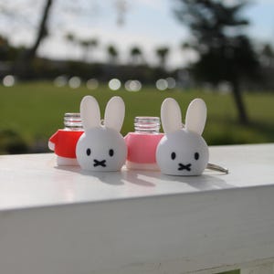 Pode incluir: Tr&ecirc;s rolhas de garrafa de coelho branco com topos vermelhos, rosa e brancos. As rolhas de coelho t&ecirc;m olhos pretos e uma boca preta.