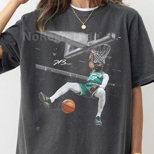 May include: Dark gray t-shirt featuring a basketball player in a green and white uniform, mid-dunk. The image includes a basketball, hoop, and the text "DB3". The shirt is a casual, oversized fit.