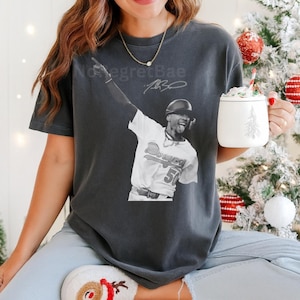 May include: Dark gray t-shirt featuring a black and white image of a baseball player in a Dodgers uniform, with the text "No Regret Bae" and a signature. The player is raising his arm in celebration.