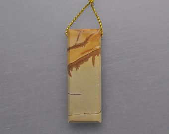 May include: A rectangular pendant with a natural stone appearance. The pendant features a blend of tan, brown, and cream colors, with a gold-colored cord attached at the top. The stone has a unique pattern and texture.