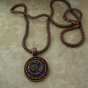 May include: A copper chain necklace with a round pendant featuring a beaded design in shades of brown and purple.