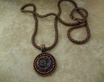 May include: A copper chain necklace with a round pendant featuring a beaded design in shades of brown and purple.