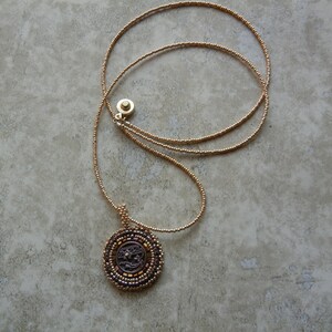 May include: A gold beaded necklace with a round, dark brown pendant featuring a detailed design.