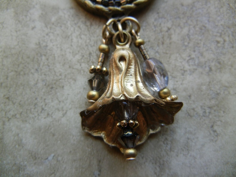 May include: A gold-tone pendant with a bell-shaped design and clear crystal accents. The pendant is adorned with small gold beads and hangs from a chain.