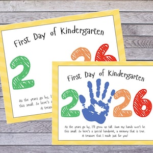 May include: Two rectangular signs with yellow chevron borders featuring the text First Day of Kindergarten. The designs include the year 2026 in green, orange, and red, with a blue handprint in the center of the year on the front sign.
