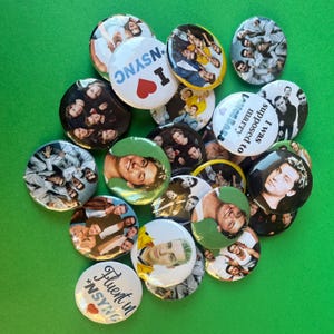 May include: A collection of round, colorful buttons featuring images of the boy band *NSYNC. Some buttons have text that reads "I *NSYNC", "Fluent in *NSYNC", and "I was supposed to marry Lance Bass". The buttons are scattered on a green surface.