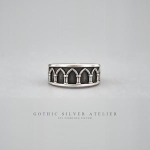 May include: A silver ring featuring a repeating architectural arch pattern with a dark, oxidized finish in the recessed areas. The band has a polished silver rim along the top and bottom edges. The text GOTHIC SILVER ATELIER 925 STERLING SILVER is below.