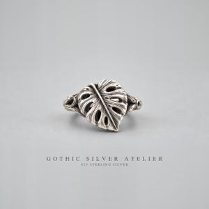 May include: A sterling silver ring featuring a detailed monstera leaf design with cutouts and textured veins. The band is integrated into the leaf structure. Below the ring, the text reads GOTHIC SILVER ATELIER and 925 STERLING SILVER.