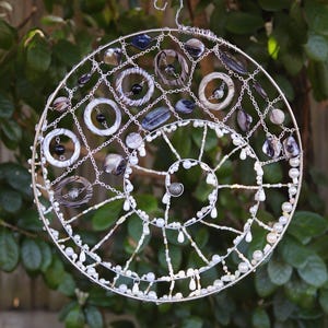 Ocean spiral seashell suncatcher hanging outdoors in natural sunlight with shells, pearls and silver wire spiral design.