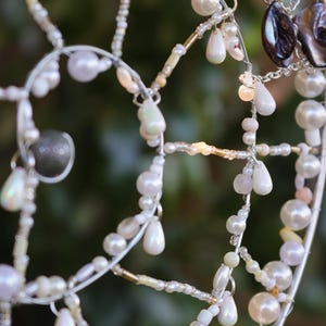 Close up of handmade coastal suncatcher showing freshwater pearls, shell rings and ocean coloured glass beads.