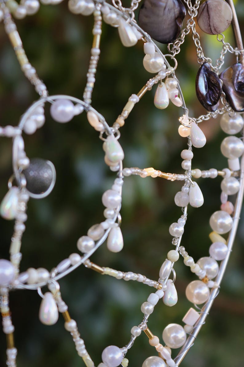 Close up of handmade coastal suncatcher showing freshwater pearls, shell rings and ocean coloured glass beads.