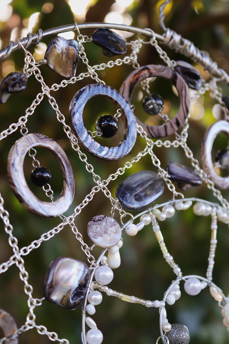 Close up of handmade coastal suncatcher showing freshwater pearls, shell rings and ocean coloured glass beads.