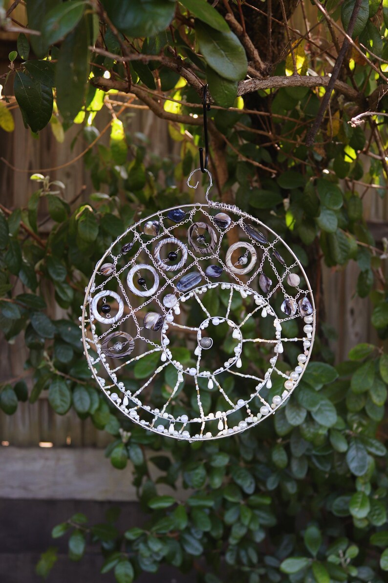 Ocean spiral seashell suncatcher hanging outdoors in natural sunlight with shells, pearls and silver wire spiral design.