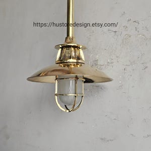Könnte beinhalten: Eine Pendelleuchte aus Messing mit rundem Schirm und Glaseinfassung. Die Leuchte hat eine goldene Oberfläche und ist an einer Messingstange aufgehängt. Der Text "https://hustoredesign.etsy.com/" ist sichtbar.