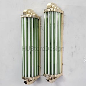 May include: Two Art Deco-style sconces with vertical green and white striped glass tubes. The sconces have gold-colored metal accents at the top and bottom. The text "HUStoreDesign" is visible on the glass.