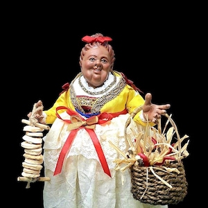 Peut inclure: Figurine détaillée d'une femme en costume traditionnel, avec un haut jaune, une jupe en dentelle blanche et un nœud rouge. Elle tient une pile d'objets ronds sur un bâton et un panier tressé rempli d'articles. La figurine a une expression souriante.