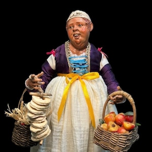 Peut inclure: Une figurine artisanale représentant une personne vêtue d'un corsage violet à lacets bleus sur une blouse blanche et d'une longue jupe blanche avec un ruban jaune. La figurine tient un panier en osier de pêches et des pains ronds.