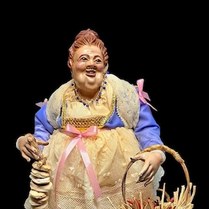 Peut inclure: Figurine détaillée d'une femme en robe jaune et bleue, tenant une pile d'objets ronds sur un bâton et un panier. La femme a une expression souriante et porte un collier et un col en dentelle. Des rubans roses ornent la robe.