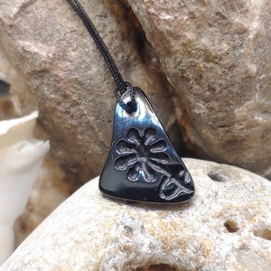May include: Black ceramic pendant with a triangular shape and a raised flower design.