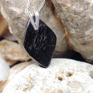 Può includere: Un ciondolo in pietra nera con una catena d'argento. Il ciondolo ha una forma di diamante con una superficie liscia e lucida.