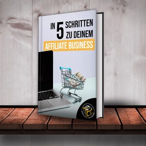 Może przedstawiać: Biała książka z tytułem "In 5 Schritten zu deinem Affiliate Business" i obrazem laptopa i w&oacute;zka sklepowego pełnego pieniędzy. Książka znajduje się na drewnianej p&oacute;łce.