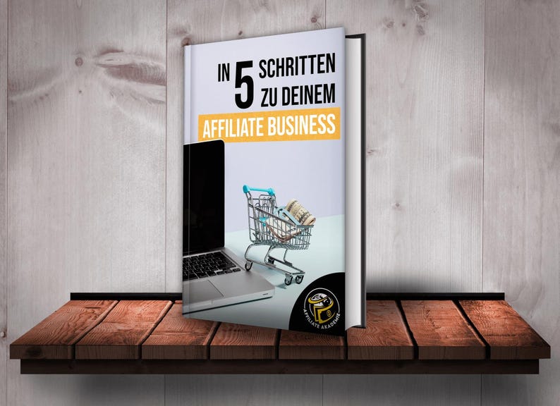 Może przedstawiać: Biała książka z tytułem "In 5 Schritten zu deinem Affiliate Business" i obrazem laptopa i w&oacute;zka sklepowego pełnego pieniędzy. Książka znajduje się na drewnianej p&oacute;łce.