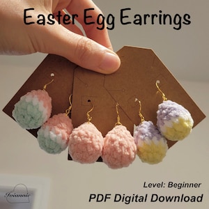 Op de afbeelding: Paasei-oorbellen, gepresenteerd op bruine kaarten. De oorbellen zijn gemaakt van zacht, getextureerd garen in pastelkleuren, waaronder roze, groen, wit, geel en paars. De tekst "Easter Egg Earrings" is zichtbaar.
