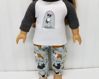 May include: A doll wearing a white and gray baseball tee with a chihuahua graphic and gray and blue pajama pants with a dog print. The text on the shirt says "Chihuahua".
