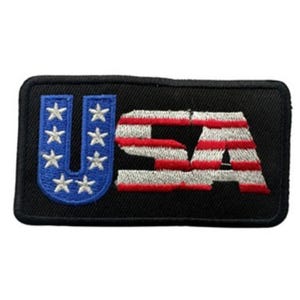 May include: Embroidered patch featuring the word "USA" in red, white, and blue. The "U" is blue with white stars, and the "SA" has red and white stripes, all on a black rectangular background.