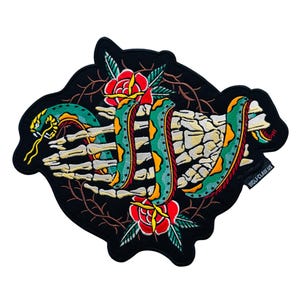 May include: Embroidered patch featuring a green and yellow snake intertwined with a skeleton hand and red roses. The design is set against a black background with thorny vines. The patch has the text "WOLF CLAW US".