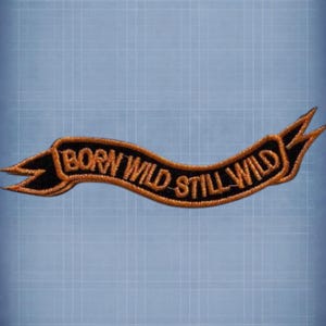 May include: Embroidered patch in a banner shape with the words "BORN WILD STILL WILD" in orange thread on a black background. The banner has pointed ends and a curved design, suitable for jackets or bags.