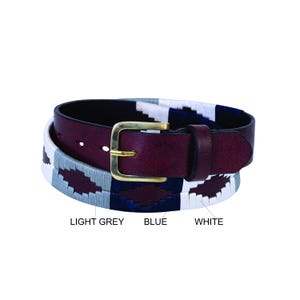 Könnte beinhalten: Ein burgunderfarbener Ledergürtel mit einer Messingschnalle. Der Gürtel hat ein gewebtes Muster in Hellgrau, Blau und Weiß. Der Text "LIGHT GREY", "BLUE" und "WHITE" ist darunter gedruckt.