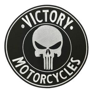 May include: Black and white embroidered patch with the words "VICTORY MOTORCYCLES" encircling a skull emblem. The skull has a stern expression with a white stitched design. The patch is circular.